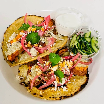 A plate with tacos, sauce, and cucumber salad.